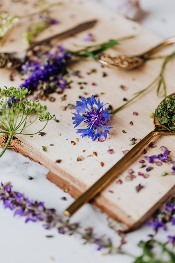 Close-up of fresh herbs and flowers with golden teaspoons on a wooden board.